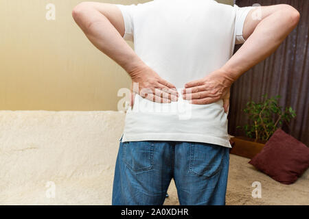 Lower back pain. Man in white shirt holding his back in pain Stock Photo