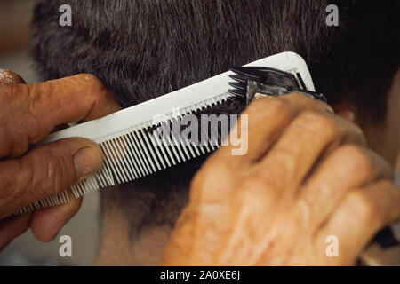 Closeup hand of hairdresser cutting hair with clipper at local barber shop. Stock Photo