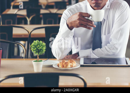 Asian Handsome businessman working outdoor in the coffee shop with laptop and holding cup of coffee on hand. Work outside office using technology with Stock Photo