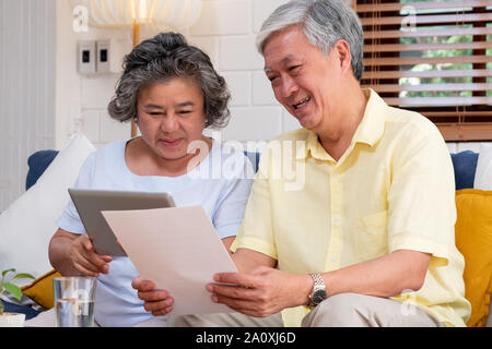 Asian senior couple use tablet searching about retirement financial document sitting on sofa at home,senior learn to use technology.aging in place con Stock Photo