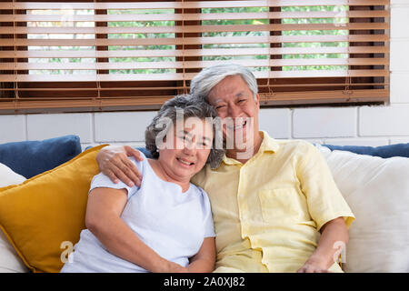Asian couple senior embracing and sitting comfortably on sofa and  watching tv in living room at home. Stock Photo
