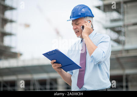 Architect manager talking on the cellphone in front of construction site Stock Photo