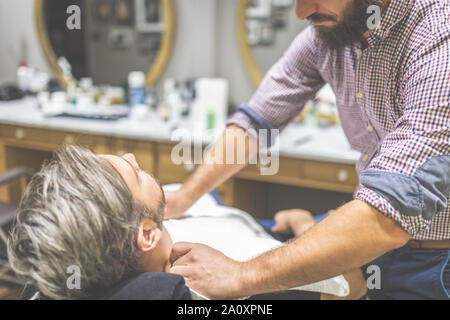 Hairdresser preparing client for shaving with towel. Man visiting barber shop. Stock Photo