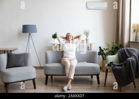 Relaxed older woman sitting on couch in air conditioner room Stock Photo