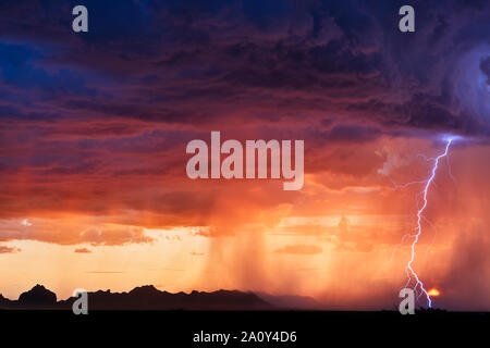A dramatic lightning bolt strikes though sunset storm clouds as a monsoon thunderstorm moves through the desert near Salome, Arizona Stock Photo