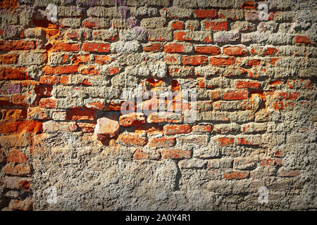 grungy damaged old red brick wall with broken plaster layer Stock Photo