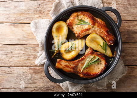 Rustic style baked pork chops with pears and rosemary in honey-garlic sauce served in a pan close-up on the table. Horizontal top view from above Stock Photo