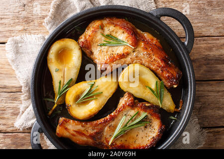 Holiday recipe for baked pork chops with pears and rosemary in honey sauce served in a pan close-up on the table. Horizontal top view from above Stock Photo