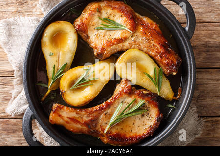 Fried pork chops with ribs with pears and rosemary in honey sauce served in a pan close-up on the table. Horizontal top view from above Stock Photo