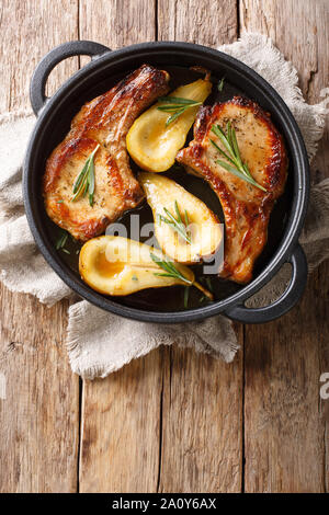 Autumn food pork chops with ribs baked with pears and rosemary in honey sauce in a pan close-up on the table. Vertical top view from above Stock Photo