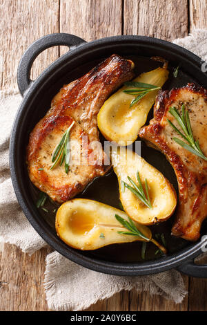 Tasty hot pork chops baked with pears and rosemary in honey sauce in a pan close-up on the table. Vertical top view from above Stock Photo