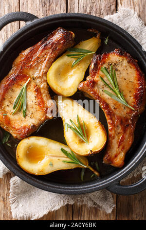 Baked pork chops with pears, rosemary and honey in a pan close-up on the table. Vertical top view from above Stock Photo