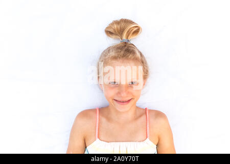 Close up portrait of adorable little girl lying on white background with stylized long blond hair Stock Photo