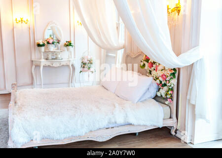 Beautiful luxury classic white bright clean interior bedroom in baroque style with king-size bed, large window, armchair and flower composition Stock Photo