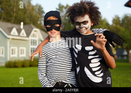 Waist up portrait of two happy boys wearing Halloween costumes looking at camera while posing outdoors, copy space Stock Photo