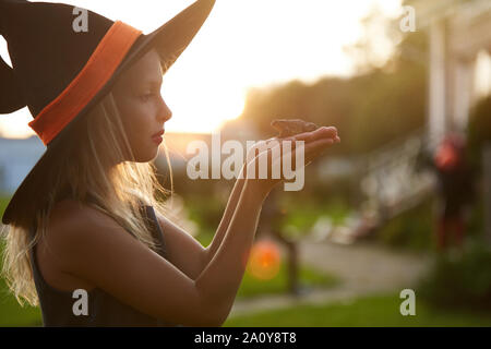 Side view portrait of cute little witch holding frog while playing outdoors in Halloween, copy space