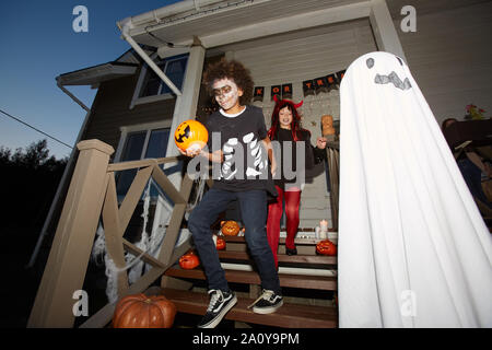 Low angle portrait of happy children leaving house trick or treating on Halloween, focus on smiling African-American boy in foreground, shot with flash Stock Photo