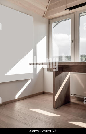 Stylish modern interior with a sloping wooden ceiling and white walls and a parquet on the floor. There is a light table and a hanging dark lamp over Stock Photo