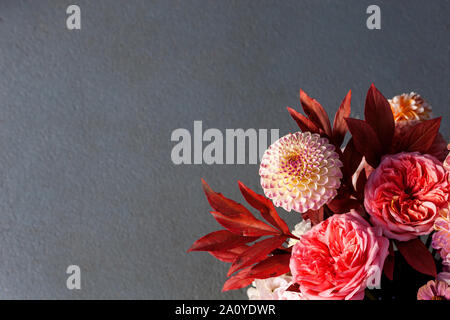 Floral composition of dahlia flowers, roses and autumn leaves. Arty, bright red and pink color  bouquet of flowers on grey background Stock Photo