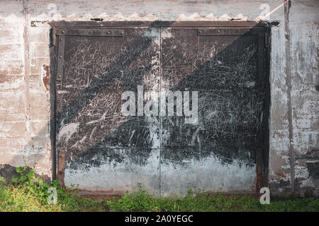 Old grunge garage door with black iron doors and iron door hinges. The gates are all scratched and scribbled. Around the plastered wall. Stock Photo