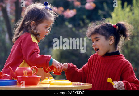 two little girls playing outdoors fighting over toy tea set Stock Photo