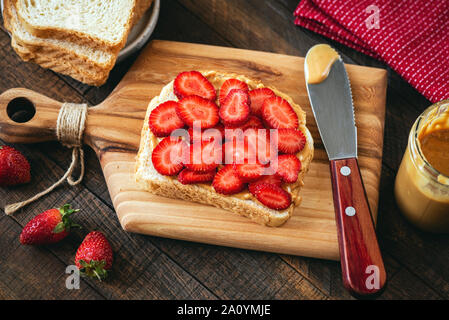 Peanut butter and strawberry toast on a wooden cutting board. Healthy breakfast or lunch sandwich Stock Photo