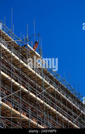 Construction worker standing on top of scaffolding, pulling up materials to the top of the building Stock Photo