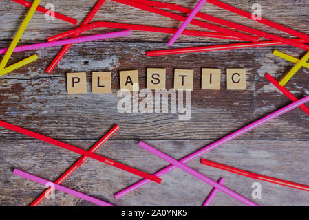 the English word plastic laid with wooden letters on a wooden background beside colored straws Stock Photo