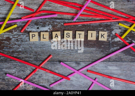 the German word for plastic laid with wooden letters on a wooden background beside colored straws Stock Photo