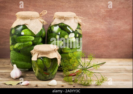 Pickled cucumbers with spices on the wooden background.Three glass jars with pickled cucumbers.Fermented food.Horizontal with copy space. Stock Photo