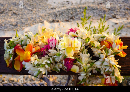 A lei of beautiful tropical flowers rests on a wooden railing above a white sandy beach Stock Photo