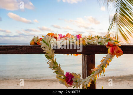 A beautiful lei of flowers rests on a the railing of a wooden deck overlooking a lagoon in French Polynesia in the South Pacific Stock Photo