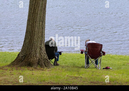 The boy is sitting on a folding chair on the shore of a lake or river.  Recreation, weekends, tourism. Rear view - a Royalty Free Stock Photo from  Photocase