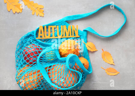 Autumn flat lay with turquoise string bag with orange pumpkins, top vie on gray stone background Stock Photo
