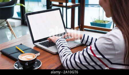 Close up woman type on laptop keyboard and looking at computer screen on table in coffee shop,Blank notebook screen mock up for display of design or c Stock Photo