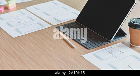 Cropped shot of UX web developer workplace with tablet and a cup of coffee on wooden table in comfortable room Stock Photo