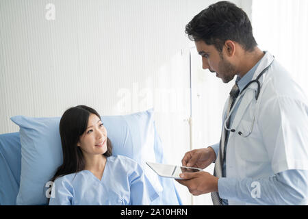 Doctor is talking with young female patient and taking notes while in his office. Stock Photo