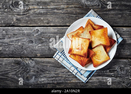 fresh toasts of wheat bread on a white plate on a wooden rustic table, horizontal view from above, free space for text, flatlay Stock Photo