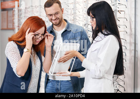 red-haired client putting on ned modern glasses , looking at the mirror at store,business concept. close up photo Stock Photo