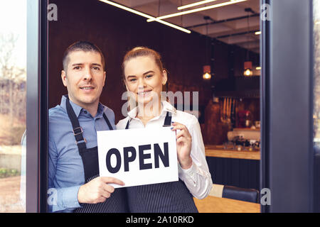Two cheerful small business owners smiling and looking at camera while standing at entrance door Stock Photo