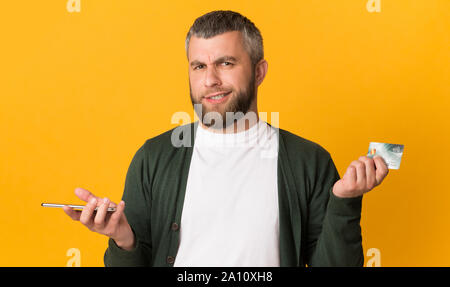 Sceptical man holding cellphone and credit card Stock Photo