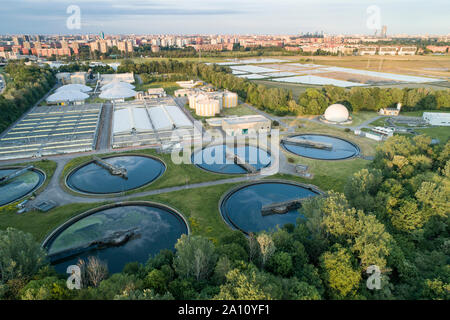 Flying over sewage treatment plant. Aerial view of industrial water treatment for the city in background. Waste water purification.