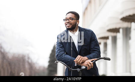 Afro businessman riding on bike to work and listening music Stock Photo