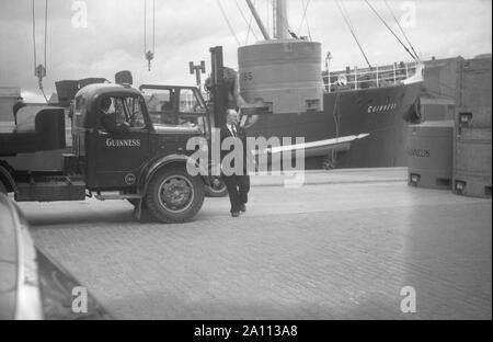 Shipping Guinness beer in giant metal beer kegs (transportable tanks) by truck to the docks to be loaded on to ships by fork-lift trucks, Dublin, Eire c. 1955 Stock Photo