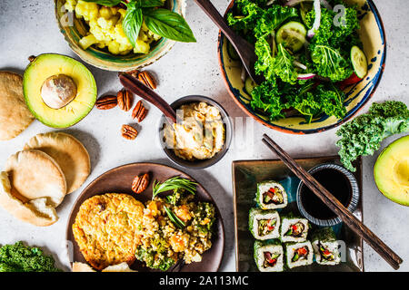 Healthy vegan food table. Flat lay of stew with chickpeas, vegan bergrer, hummus, kale salad, vegan sushi rolls and bread. Stock Photo