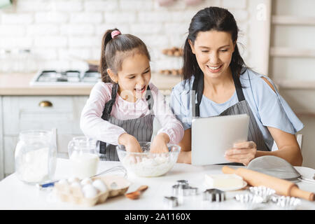 Mother and daughter using digital tablet in kitchen, looking recipe Stock Photo