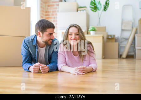 Young beautiful couple in love relaxing lying on the floor together with cardboard boxes around for moving to a new house Stock Photo