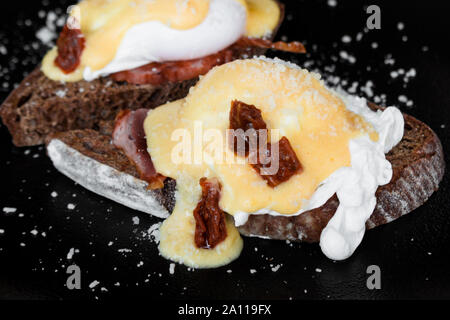 Cereal toast with fried bacon, egg Benedict and sun-dried tomato. Gourmet Breakfast with a poached egg. Stock Photo