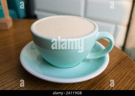 Turquoise Cup of coffee on a wooden table in the cafe. A Cup of lavender Rafe against a white brick wall. Stock Photo