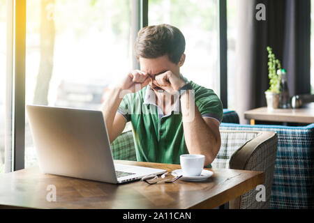 Young sad alone businessman in green t-shirt sitting with laptop, holding head down and rub his eyes, or crying. business and freelancing problem conc Stock Photo